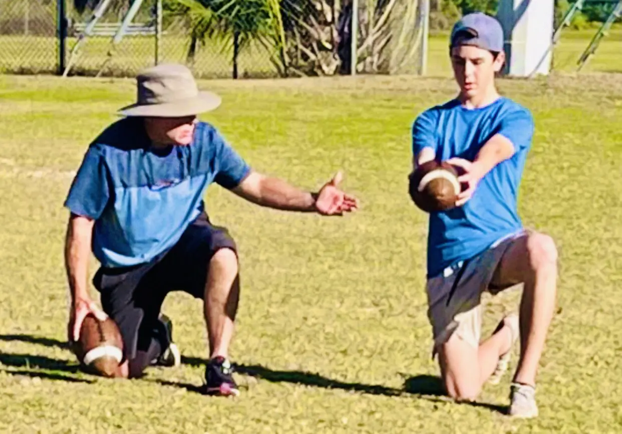 Coach demonstrating football hold to young player