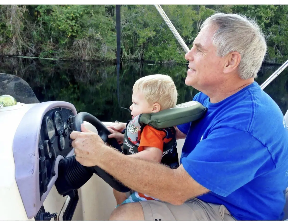 Senior man teaching toddler to steer boat