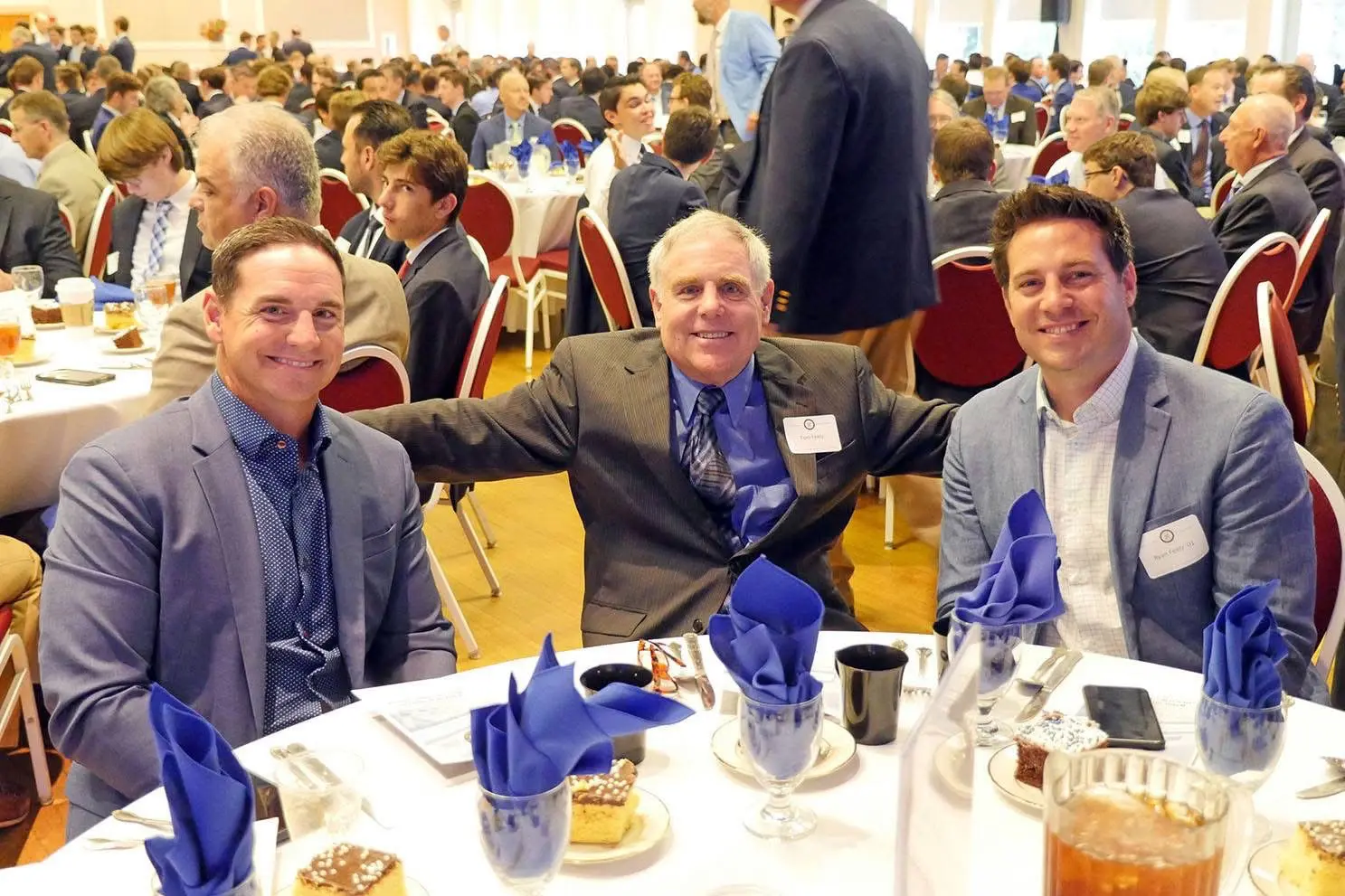 Three men in suits smiling at banquet