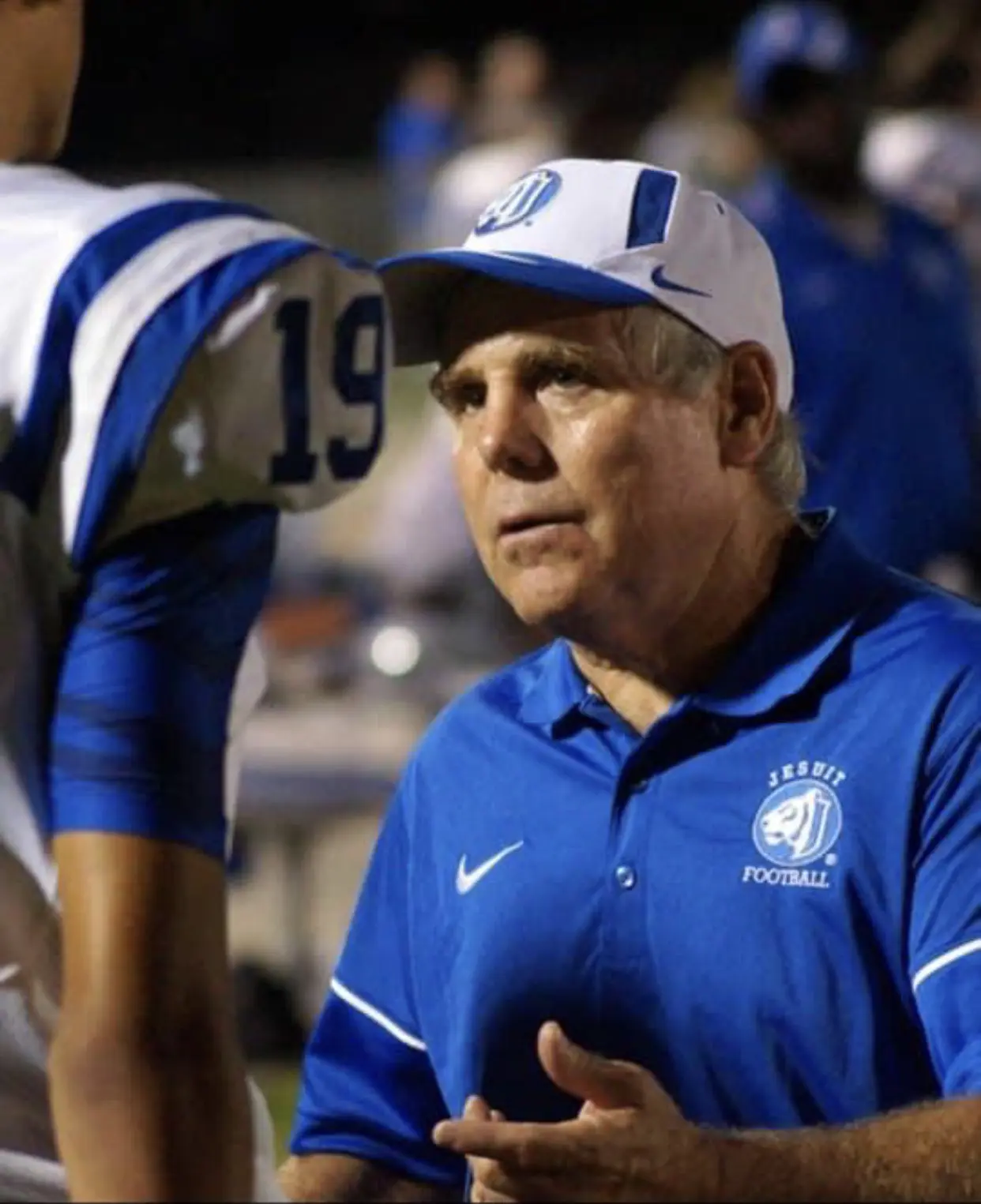 Football coach in blue polo instructing player