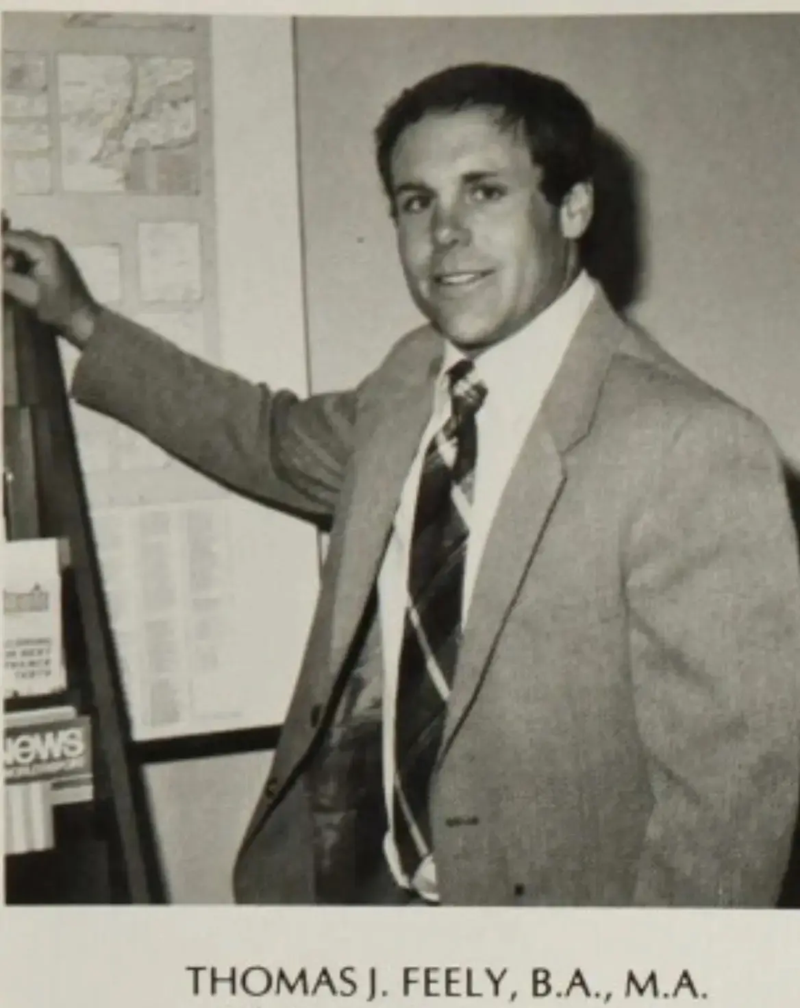 Black and white photo of a man in a suit posing by a display board.
